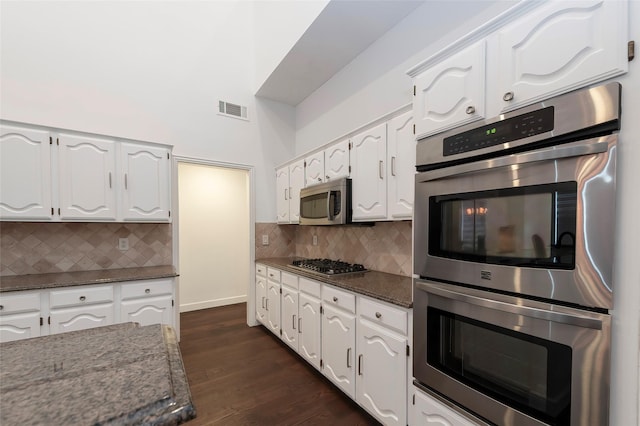 7100 Oakbrook Dr, Plano, TX 75025 - kitchen featuring stainless steel appliances, white cabinets, dark stone countertops, backsplash, and a towering ceiling