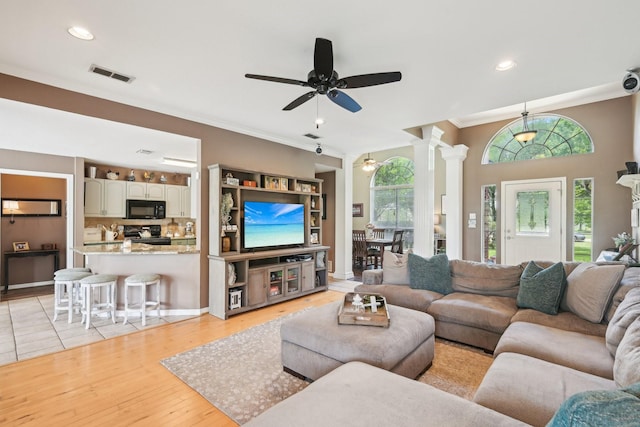 living room featuring ornate columns, crown molding, plenty of natural light, a ceiling fan, and light wood finished floors