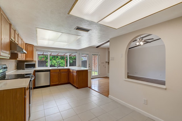 932 Goodwin Dr, Plano, TX 75023 - kitchen featuring appliances with stainless steel finishes, a peninsula, under cabinet range hood, brown cabinetry, and light countertops