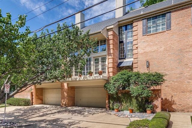 view of home's exterior with brick siding, a chimney, driveway, a balcony, and a garage