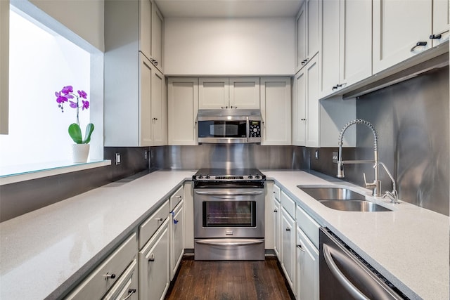 kitchen with appliances with stainless steel finishes, a sink, dark wood-style flooring, and light stone counters