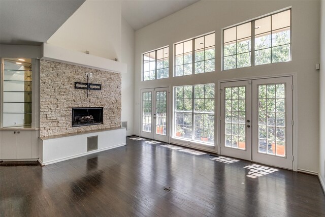 unfurnished living room with french doors, a towering ceiling, dark wood-style floors, and a stone fireplace