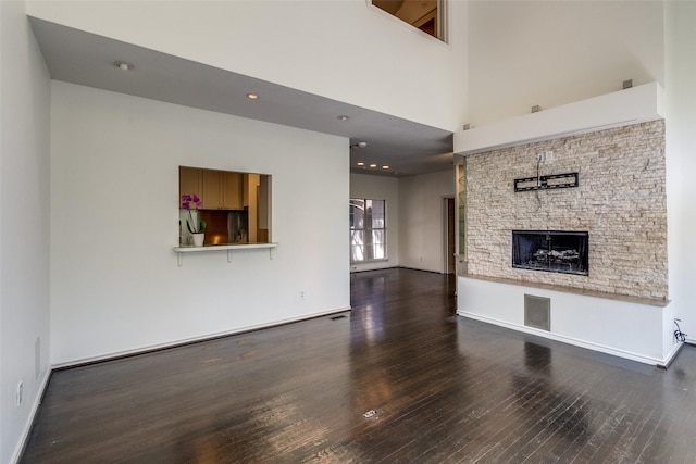 unfurnished living room with wood finished floors, a stone fireplace, a towering ceiling, baseboards, and recessed lighting