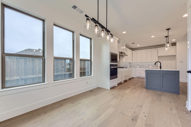1717 Truro Ln, Fort Worth, TX 76052 - kitchen with oven, white cabinetry, decorative backsplash, stainless steel microwave, and light wood-type flooring
