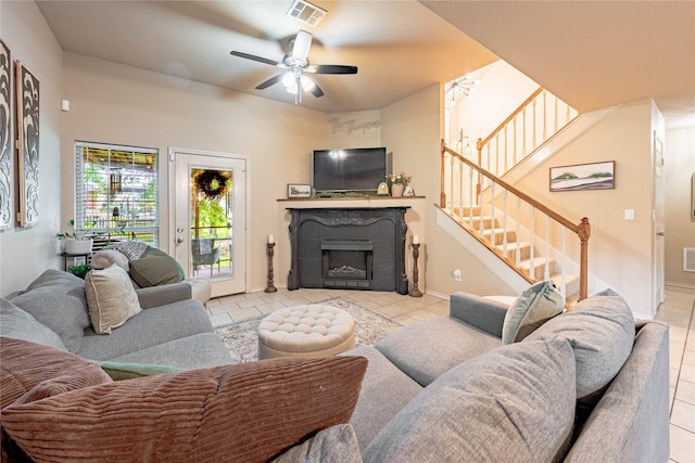 tiled living room featuring a fireplace, a ceiling fan, and stairs