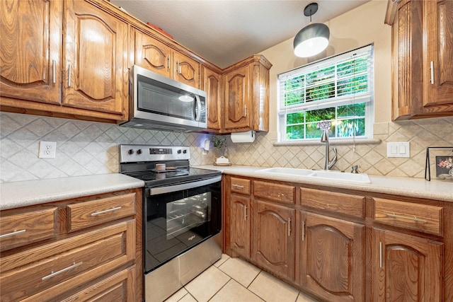 kitchen featuring stainless steel appliances, a sink, brown cabinetry, light tile patterned flooring, and decorative backsplash