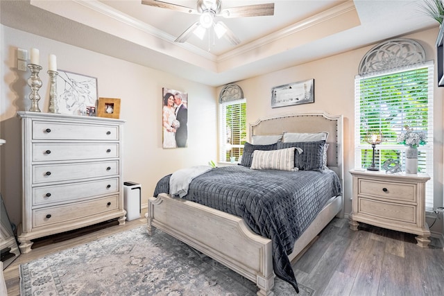 bedroom with ornamental molding, wood finished floors, a tray ceiling, and a ceiling fan