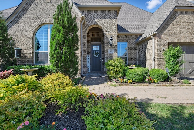 view of exterior entry with brick siding and a shingled roof