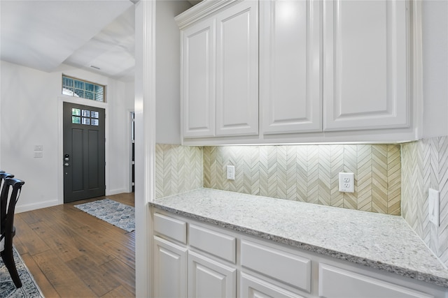 kitchen featuring white cabinetry, baseboards, dark wood-type flooring, backsplash, and light stone countertops