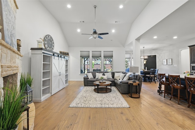 living room featuring a barn door, light wood-style flooring, a stone fireplace, vaulted ceiling, and a ceiling fan