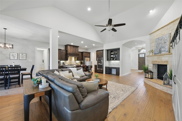 living area featuring a ceiling fan, arched walkways, a fireplace, high vaulted ceiling, and a chandelier