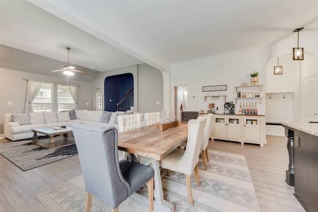 dining area featuring arched walkways, light wood-type flooring, ceiling fan, and lofted ceiling