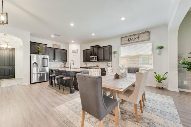 dining area with arched walkways, light wood-style floors, recessed lighting, baseboards, and crown molding