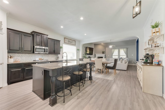 kitchen with appliances with stainless steel finishes, open floor plan, decorative backsplash, a breakfast bar area, and light wood-style floors