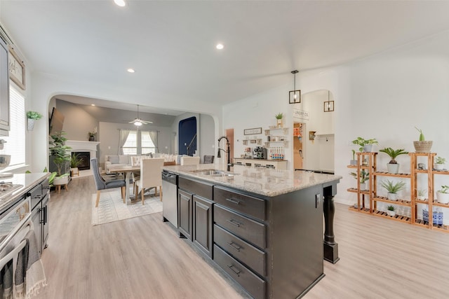 kitchen with appliances with stainless steel finishes, arched walkways, a sink, light wood finished floors, and a ceiling fan