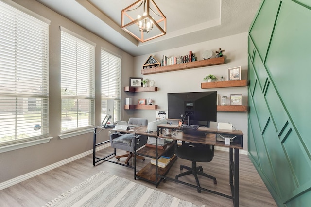 office space featuring light wood-style floors, baseboards, a tray ceiling, and a chandelier