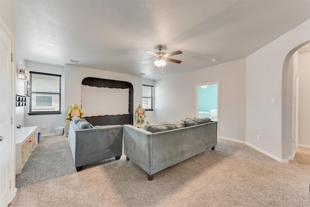 living area with arched walkways, plenty of natural light, a ceiling fan, a textured ceiling, and light colored carpet