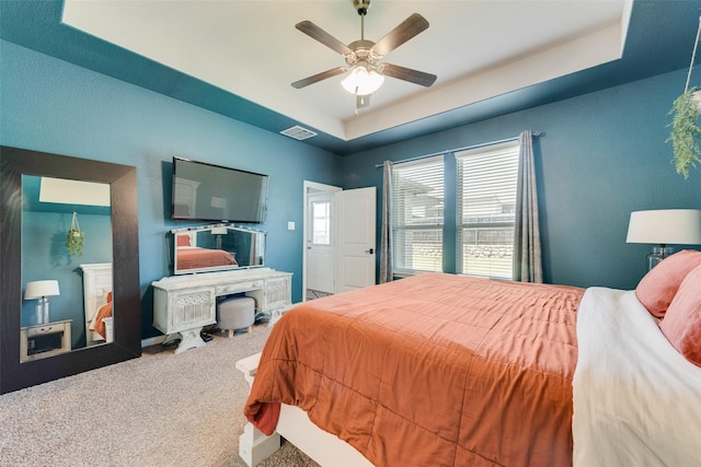 bedroom with a raised ceiling, carpet floors, and a ceiling fan