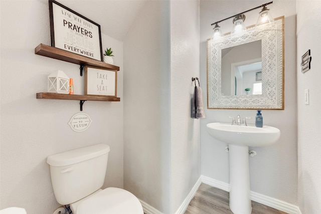 half bathroom with wood finished floors, toilet, baseboards, and a sink