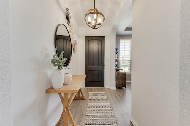 foyer with a chandelier, wood finished floors, arched walkways, baseboards, and crown molding