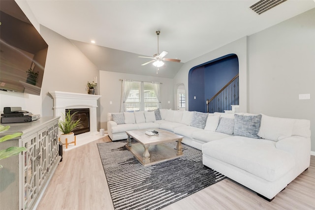 living room featuring wood finished floors, a ceiling fan, a glass covered fireplace, stairs, and lofted ceiling