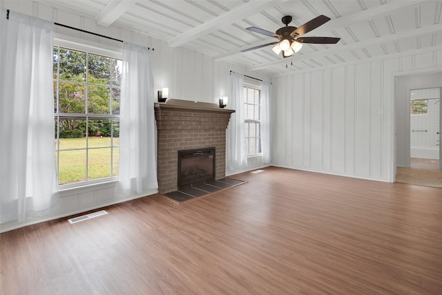1501 W Day St, Denison, TX 75020 - unfurnished living room with light wood-type flooring, a brick fireplace, a ceiling fan, beam ceiling, and a decorative wall