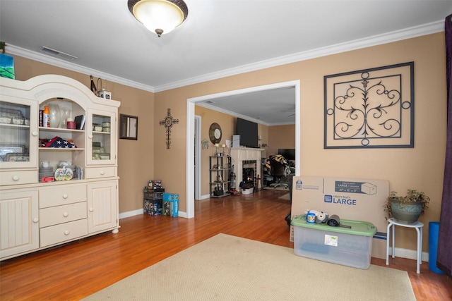 living area featuring wood finished floors, crown molding, a fireplace, and baseboards