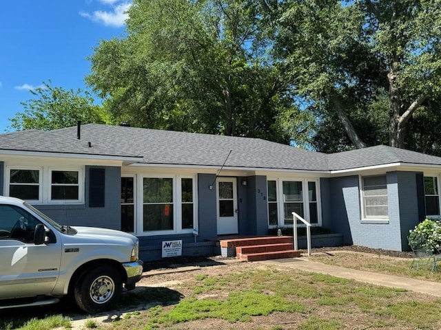 single story home featuring roof with shingles and brick siding