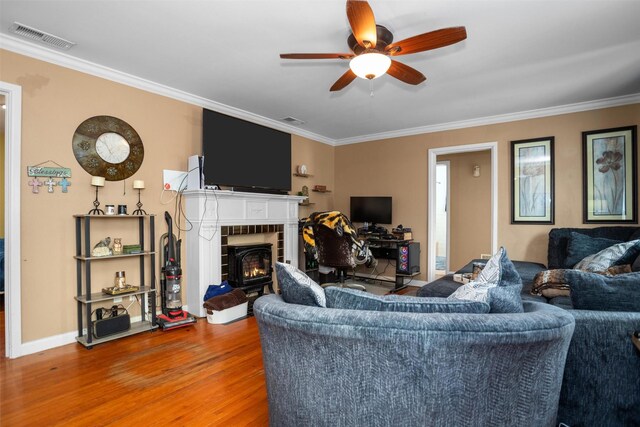 living area with crown molding, wood finished floors, ceiling fan, and a warm lit fireplace