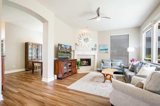 9121 Rio Blanco Dr, Frisco, TX 75033 - living room featuring light wood finished floors, ceiling fan, a tiled fireplace, arched walkways, and baseboards