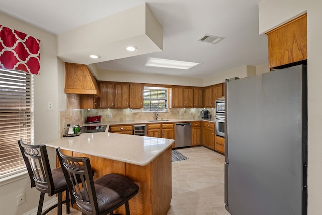 508 Quail Crest Dr, Colleyville, TX 76034 - kitchen featuring stainless steel appliances, a sink, a peninsula, brown cabinetry, and wine cooler
