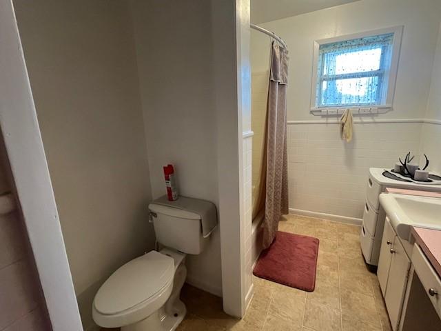 bathroom featuring washing machine and dryer, toilet, vanity, a wainscoted wall, and tile patterned floors