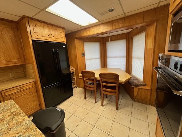 kitchen with black appliances, light countertops, light tile patterned floors, brown cabinetry, and wood walls
