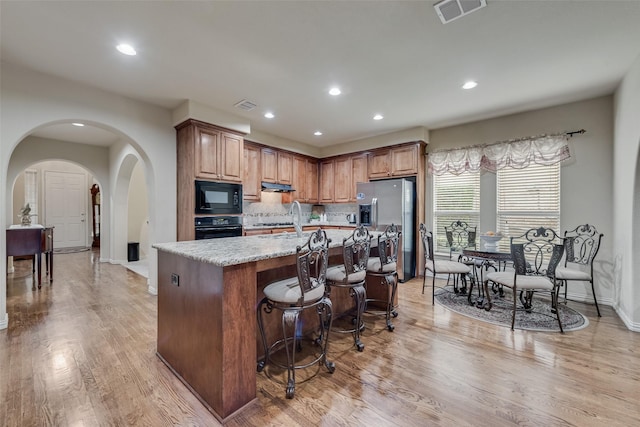 7817 Harvest Hill Ln, Mckinney, TX 75071 - kitchen with arched walkways, black appliances, decorative backsplash, light wood-type flooring, and an island with sink