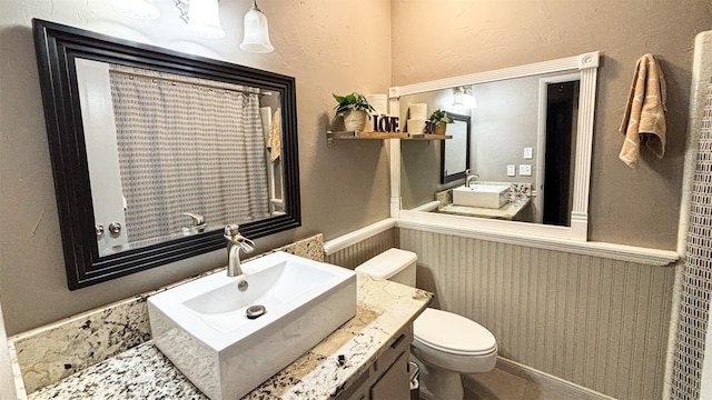 bathroom featuring toilet, vanity, and wainscoting