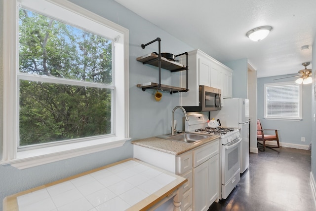 kitchen with white gas stove, stainless steel microwave, a sink, light countertops, and white cabinets