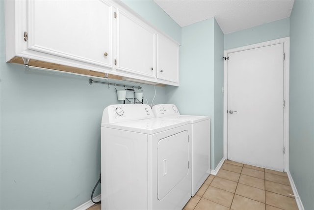 clothes washing area featuring cabinet space, washing machine and dryer, baseboards, and light tile patterned flooring