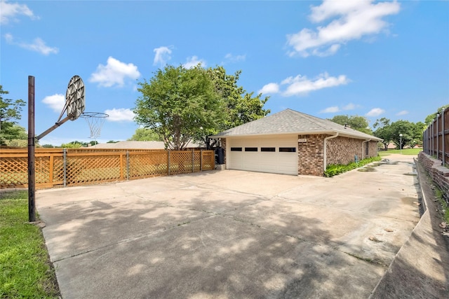 view of side of home featuring fence, concrete driveway, brick siding, and a shingled roof