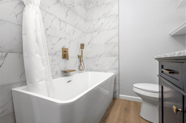 bathroom with wood finished floors, a tub to relax in, toilet, and vanity