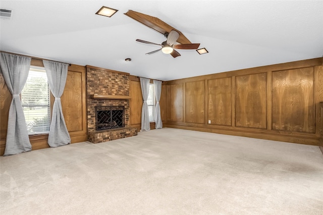 unfurnished living room featuring lofted ceiling, carpet, ceiling fan, a brick fireplace, and wooden walls