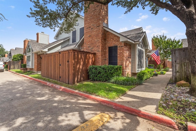 449 Harris St Unit 102D, Coppell, TX 75019 - view of home's exterior with brick siding, fence, a shingled roof, and a chimney