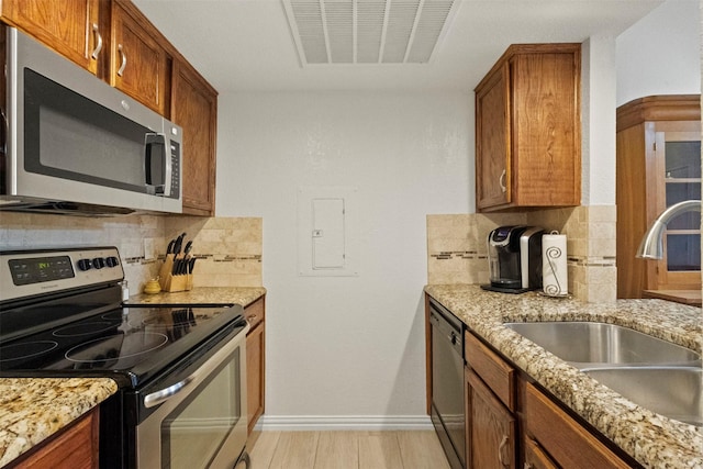 449 Harris St Unit 102D, Coppell, TX 75019 - kitchen with appliances with stainless steel finishes, a sink, backsplash, brown cabinetry, and baseboards