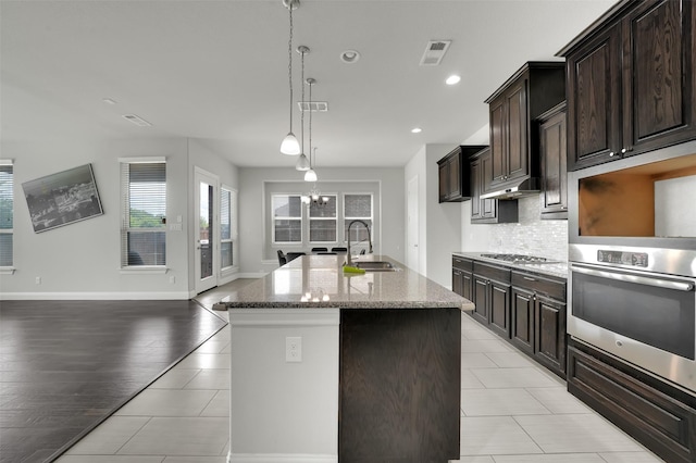 kitchen with appliances with stainless steel finishes, a sink, tasteful backsplash, light stone counters, and a kitchen island with sink