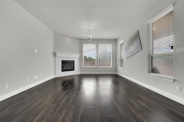 unfurnished living room featuring a chandelier, dark wood-style flooring, baseboards, and a glass covered fireplace