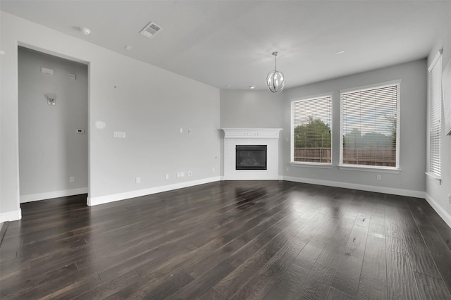 unfurnished living room with dark wood-style floors, a chandelier, a glass covered fireplace, and baseboards
