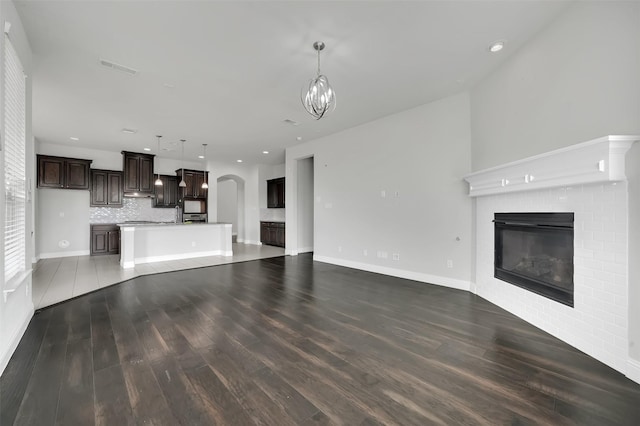 unfurnished living room with a glass covered fireplace, arched walkways, wood finished floors, recessed lighting, and baseboards
