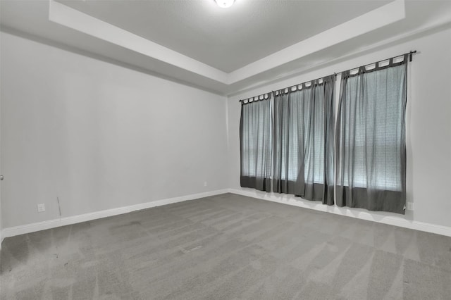 spare room with a tray ceiling, carpet floors, and baseboards