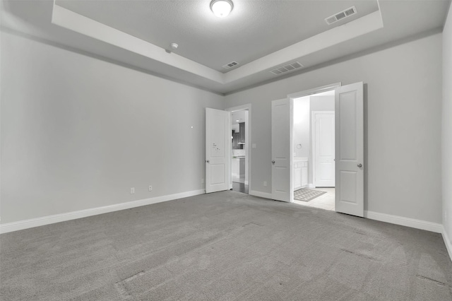 unfurnished bedroom with a raised ceiling, carpet floors, baseboards, and ensuite bathroom