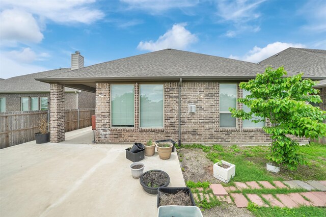 back of property with brick siding, fence, a patio, a shingled roof, and a chimney