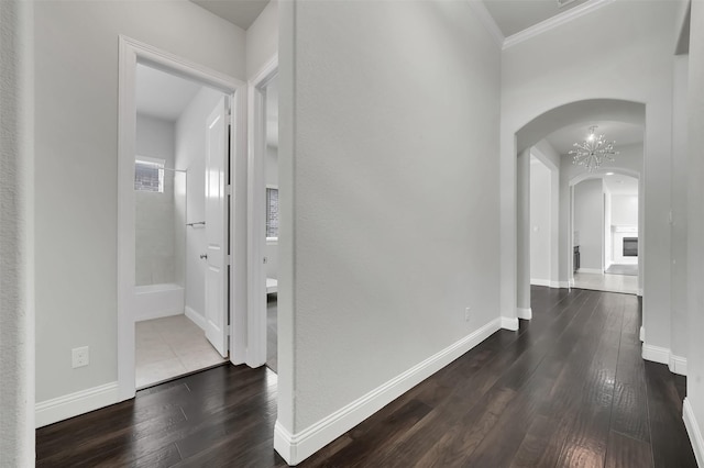 corridor featuring arched walkways, dark wood-style floors, crown molding, and baseboards